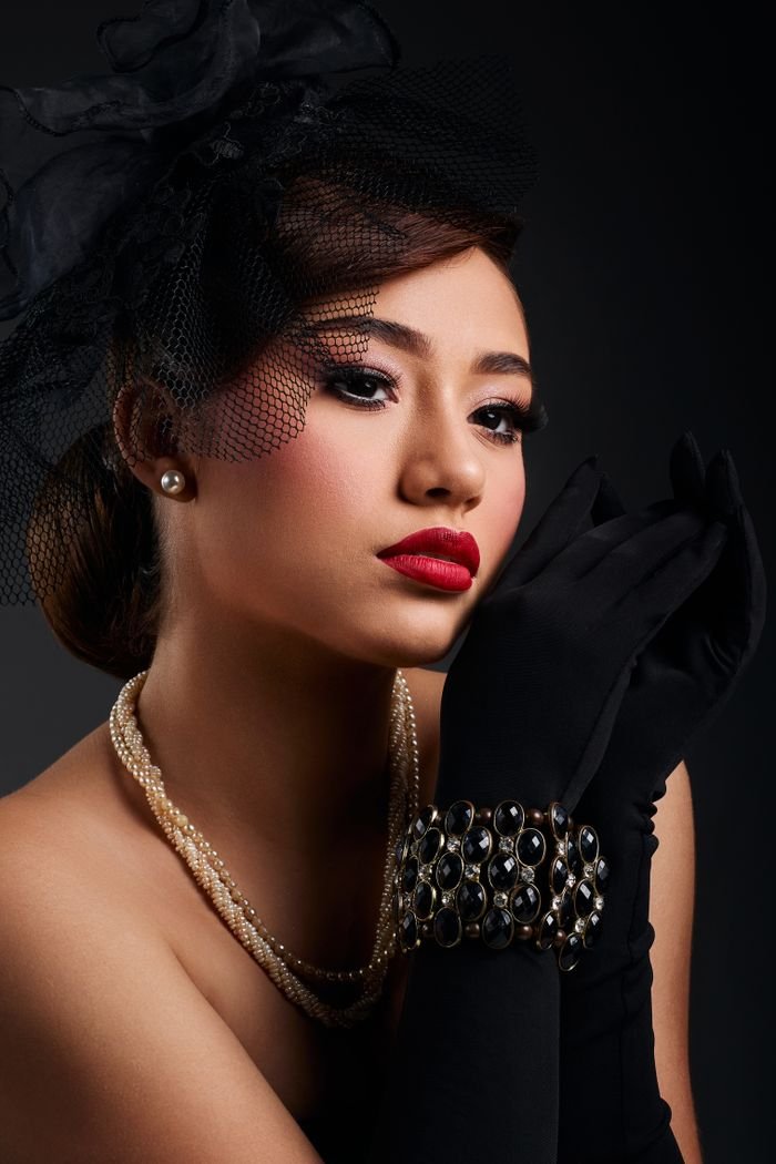 Sophisticated woman in vintage fashion with pearls and gloves posing dramatically.